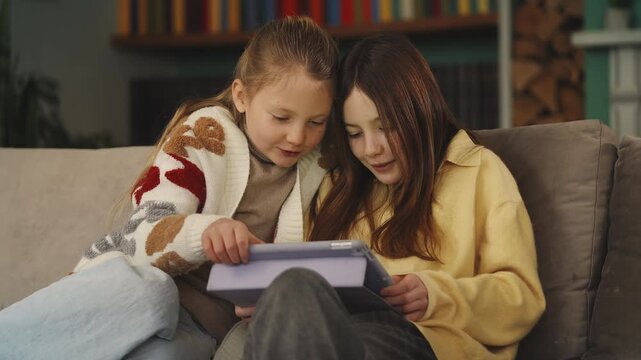 Two happy girls play educational game on tablet, enjoying learning app