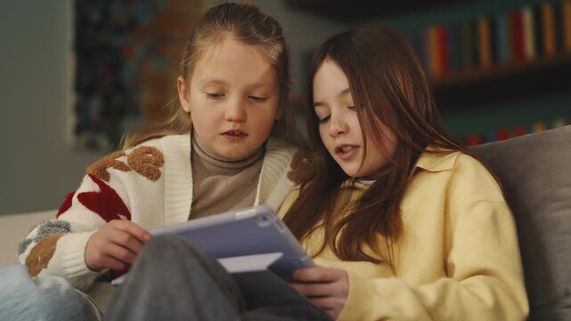 Best friends play educational game on tablet at home, interactive learning