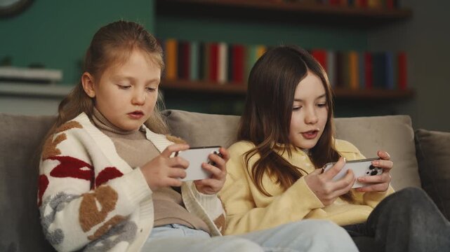 Two happy sisters play online game on phones, excessive gadget use