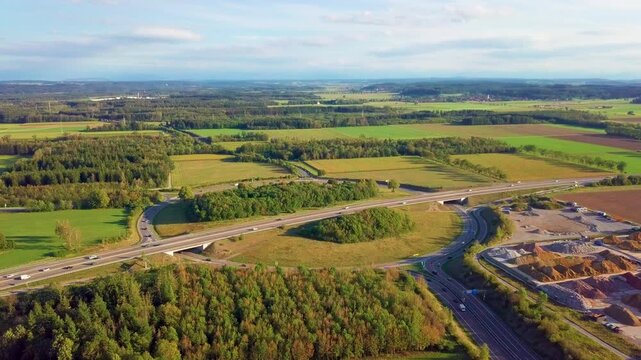Drone footage of Germany's largest roundabout near Landsberg am Lech during a warm late summer evening, featuring traffic flowing through the massive highway intersection surrounded by rural landscape