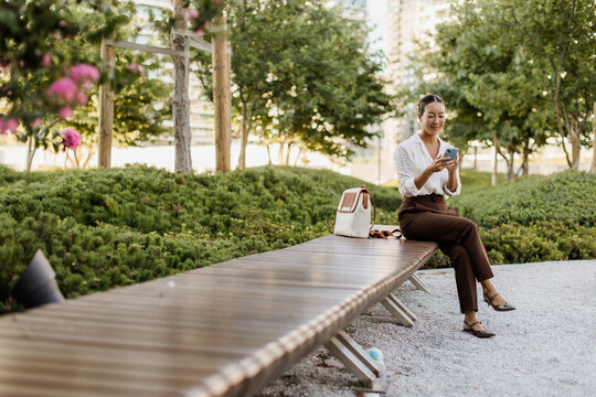 Korean woman enjoying a sunny day in a serene park while using her phone