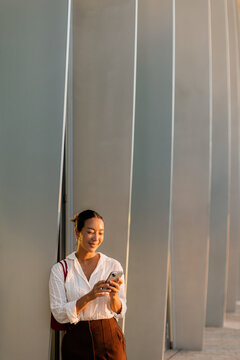 Korean woman checks her phone on a sunny day by modern architecture