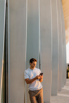 Young man engaged with his phone by a modern architectural structure