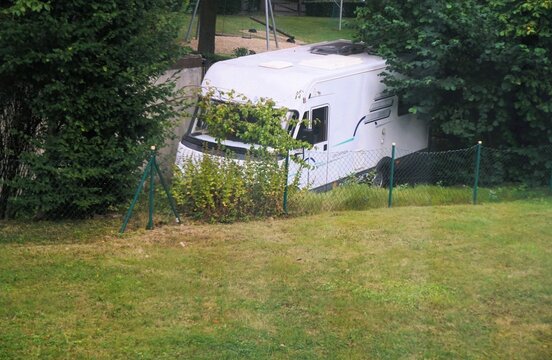 Gr&uuml;nes Gartenpanorama mit Wiese, B&auml;umen, B&uuml;schen und Zaun vor gro&szlig;em wei&szlig;en parkendem Wohnmobil am Nachmittag im Sommer