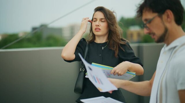 Two business people review project documents and collaborate in an outdoor urban setting. Professional colleagues analyze data and timelines together on a modern rooftop.