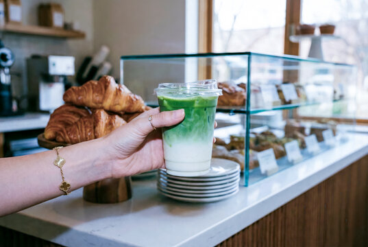 Hand holding iced matcha latte at bakery counter