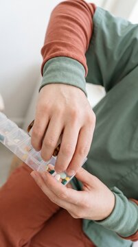 Close up hands sorting medication into weekly pill organizer container