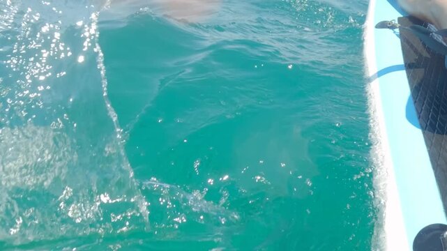 First person view of paddling on a stand up paddleboard across clear turquoise ocean water
