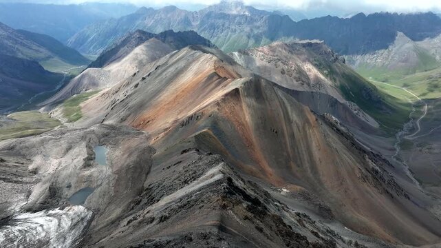 Aerial view of Chon Ashu Pass featuring rugged mountain slopes, glacial remnants, and winding roads in the high altitude landscape of Karakol, Issyk-Kul Region, Kyrgyzstan.
