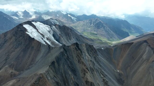 Aerial view of Chon Ashu Pass in the Tian Shan mountains, showcasing rugged rocky peaks, patches of snow, and deep valleys in Karakol, Issyk-Kul Region, Kyrgyzstan.