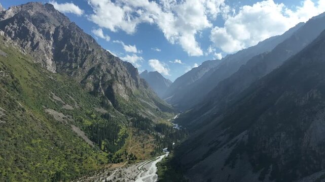 Aerial view of Ala Archa National Park with a winding river through the mountain valley surrounded by rocky slopes and evergreen forests in Bishkek, Chuy Region, Kyrgyzstan.