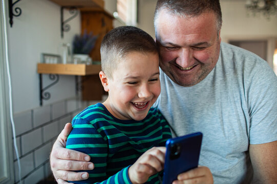 Father and son laughing together over smartphone at home