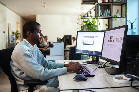 Man typing on dual monitors in modern office