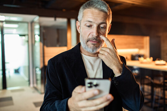 Mature man checking smartphone in modern office