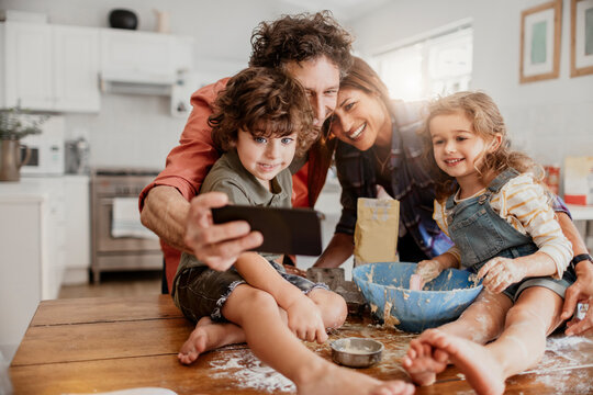 Parents taking selfie with children while baking in home kitchen