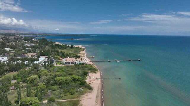 Aerial view of the sandy beach and wooden piers along the shore of Issyk Kul lake in Cholpon Ata, Issyk-Kul Region, Kyrgyzstan.