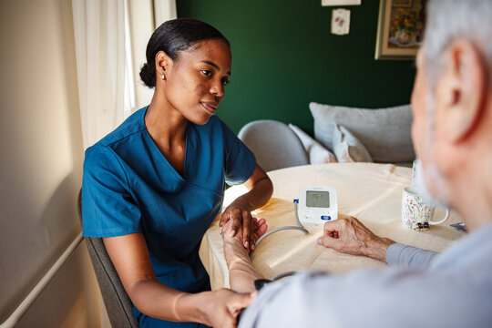 Home nurse checking senior's blood pressure at dining table