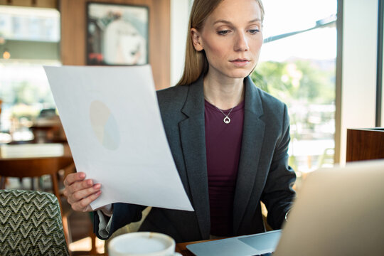 Professional woman reviewing report on laptop at cafe