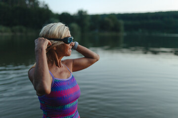 Fototapeta premium Active senior woman swimming in natural lake during indian summer.