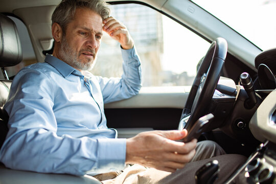 Concerned businessman reading smartphone in car
