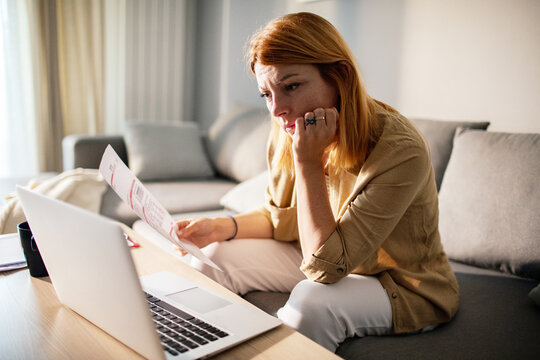 Worried woman reviewing bills on laptop at home