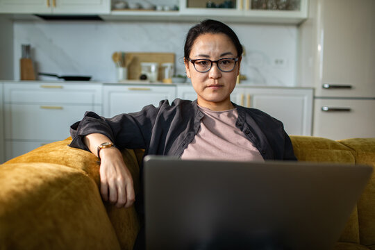 Focused woman using laptop on sofa in home kitchen