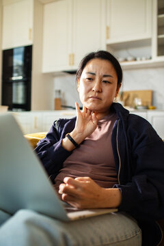 Concerned woman checking pulse during telehealth on laptop in home kitchen
