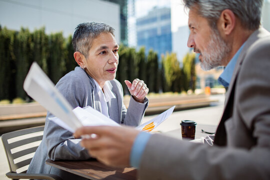 Senior business colleagues discussing financial reports at outdoor cafe