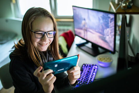 Smiling teen girl gamer playing mobile game at home desk