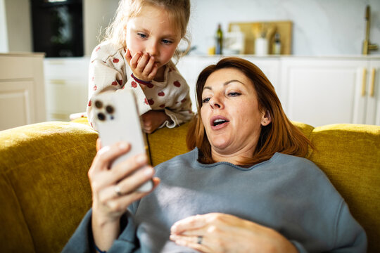 Mother and daughter watching smartphone on sofa at home