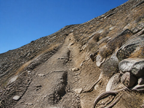 Steep unpaved trail on dry rocky hillside with ruts and exposed roots, arduous hiking path concept