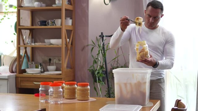 High quality continuous long take of a focused male beekeeper carefully scooping and packing premium raw mountain honey into a clear retail jar.