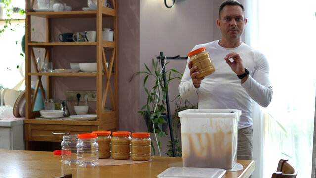 Proud local entrepreneur in clean white apparel presenting a finished jar of raw mountain honey, approving its absolute gourmet quality with a passionate chef kiss hand sign.