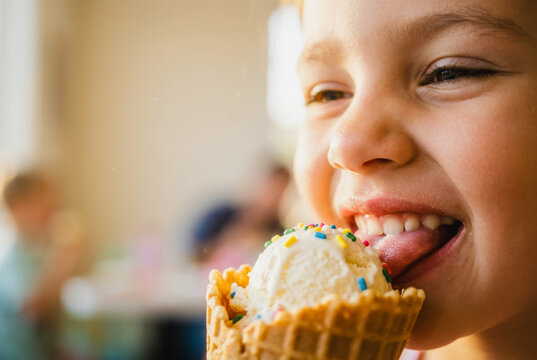 Child eating vanilla ice cream in a waffle cone with sprinkles