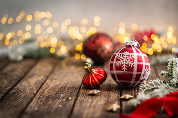 Naklejka premium A Christmas background featuring red baubles with golden glitter stripes, a star ornament, and frosted pine on a wide rustic wood table, warmly lit with twinkling lights and copy space.