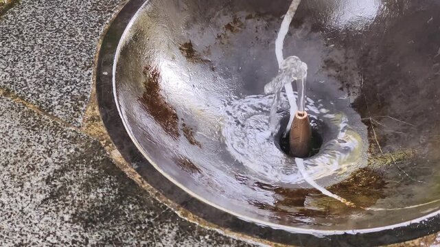 Top down view shows stone fountain basin with water stream close up. Running water stream offers vital hydration during extreme heatwave and El Nino summer weather in urban public space outdoors.