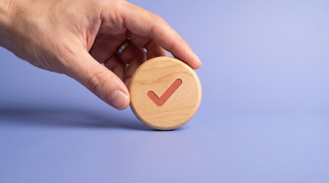 Hand holding wooden checkmark token on purple background