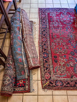 Rolled and unrolled antique Persian wool rugs on tiled floor