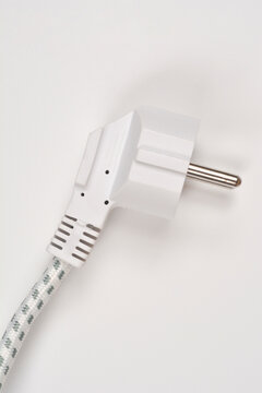 A detailed vertical studio shot of a white european schuko power plug connected to a braided fabric cord against a light background.