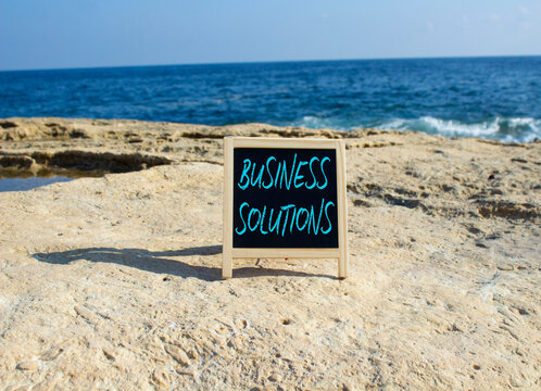 Business Solutions symbol. Blackboard with Concept words Business Solutions. Beautiful sea background. Business and Business Solutions concept. Copy space.