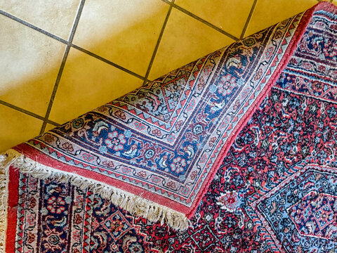 Folded corner of antique Persian wool rug on tiled floor