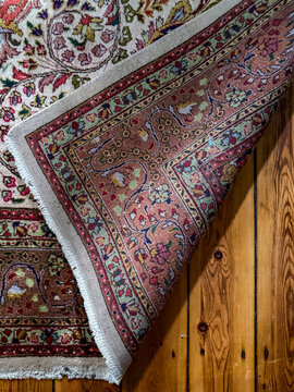 Folded corner of antique Persian wool rug on wooden floor