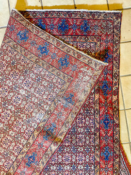 Folded corner of antique Persian wool rug on tiled floor