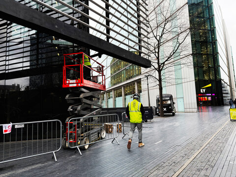 Construction worker in high vis on a scissor lift beside modern glass office buildings in London UK urban plaza
