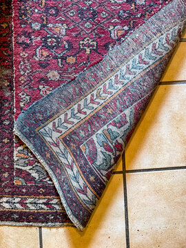 Folded corner of antique Persian wool rug on tiled floor