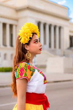 Latina woman with floral crown and traditional huipil dress, standing in front of the Capitolio building in Havana, Cuba, celebrating cultural heritage