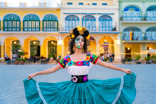 Young woman portraying a Catrina with skull makeup and traditional embroidered dress, standing in a vibrant square in Old Havana, celebrating Mexican traditions in Cuba