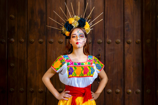 Latina woman with half sugar skull makeup and a flower headdress wearing a colorful embroidered traditional dress, celebrating Mexican Day of the Dead