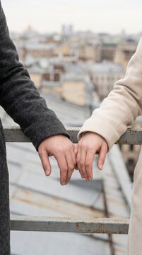Couple holding hands together on railing overlooking rooftop city skyline