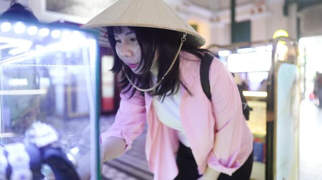 Female traveler wearing Vietnamese conical hat browsing souvenir display at Saigon Central Post Office in Ho Chi Minh City